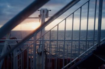 Sunset, seen through the porthole of a ferry, with some stairs and scaffolding in the foregound and the sea in the background. It looks a bit soft and and dreamy.