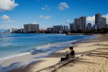 A woman looking at her phone sitting on Waikiki beach in the morning
