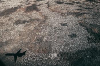 Shadow of a small passenger airliner coming in over a dark lava field with sparse vegetation