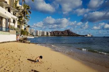 A boy playing on a section of Waikiki beach, with the Diamond Head crater in the background