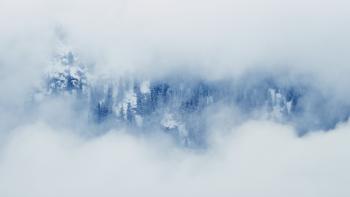 View of a snowy mountain with pine trees, through a hole in the clouds