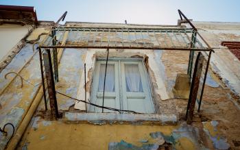 A balcony, lacking floor. Flaking paint on the building in the background.